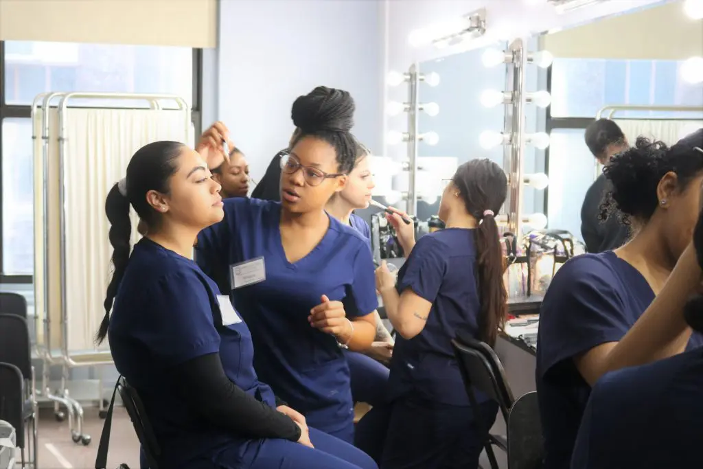 An Atelier Esthetique student providing makeup to another student, an example of the cross between cosmetology and esthetics.