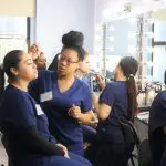 An Atelier Esthetique student providing makeup to another student, an example of the cross between cosmetology and esthetics.